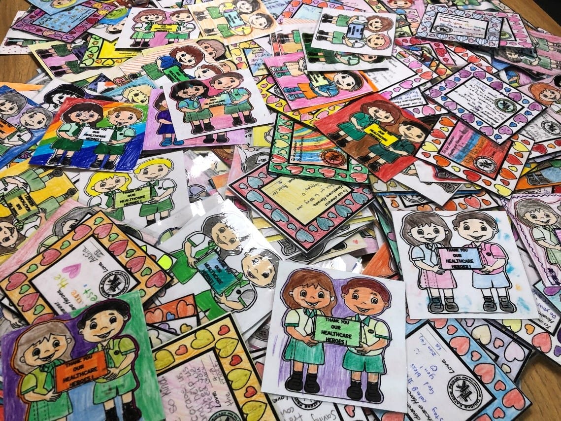 Dozens of colorful hand-drawn children's cards saying "Thank You Our Healthcare Heroes" spread across a table.